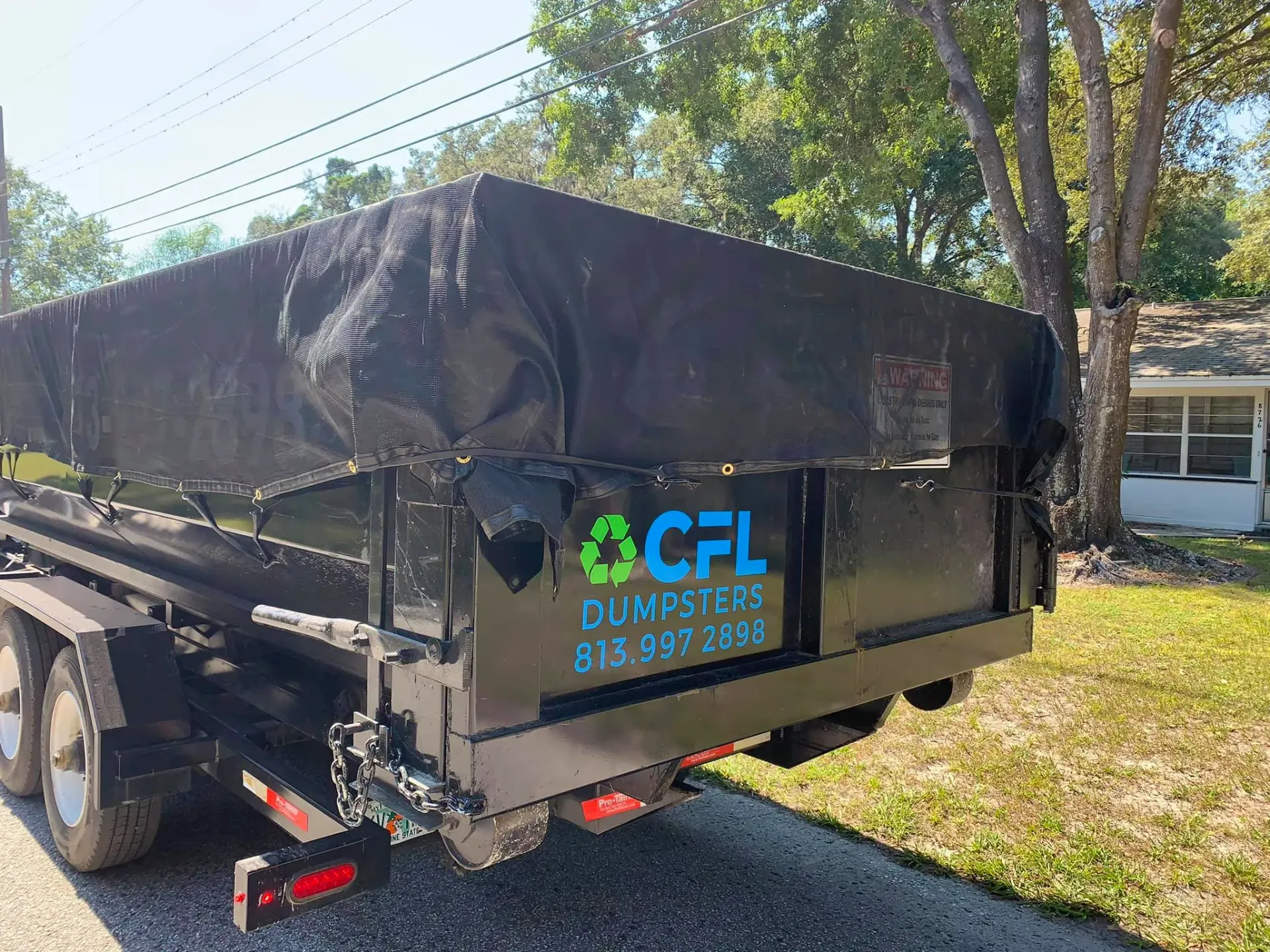 A dumpster is parked on the side of the road next to a house.