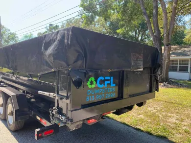 A dumpster is parked on the side of the road next to a house.