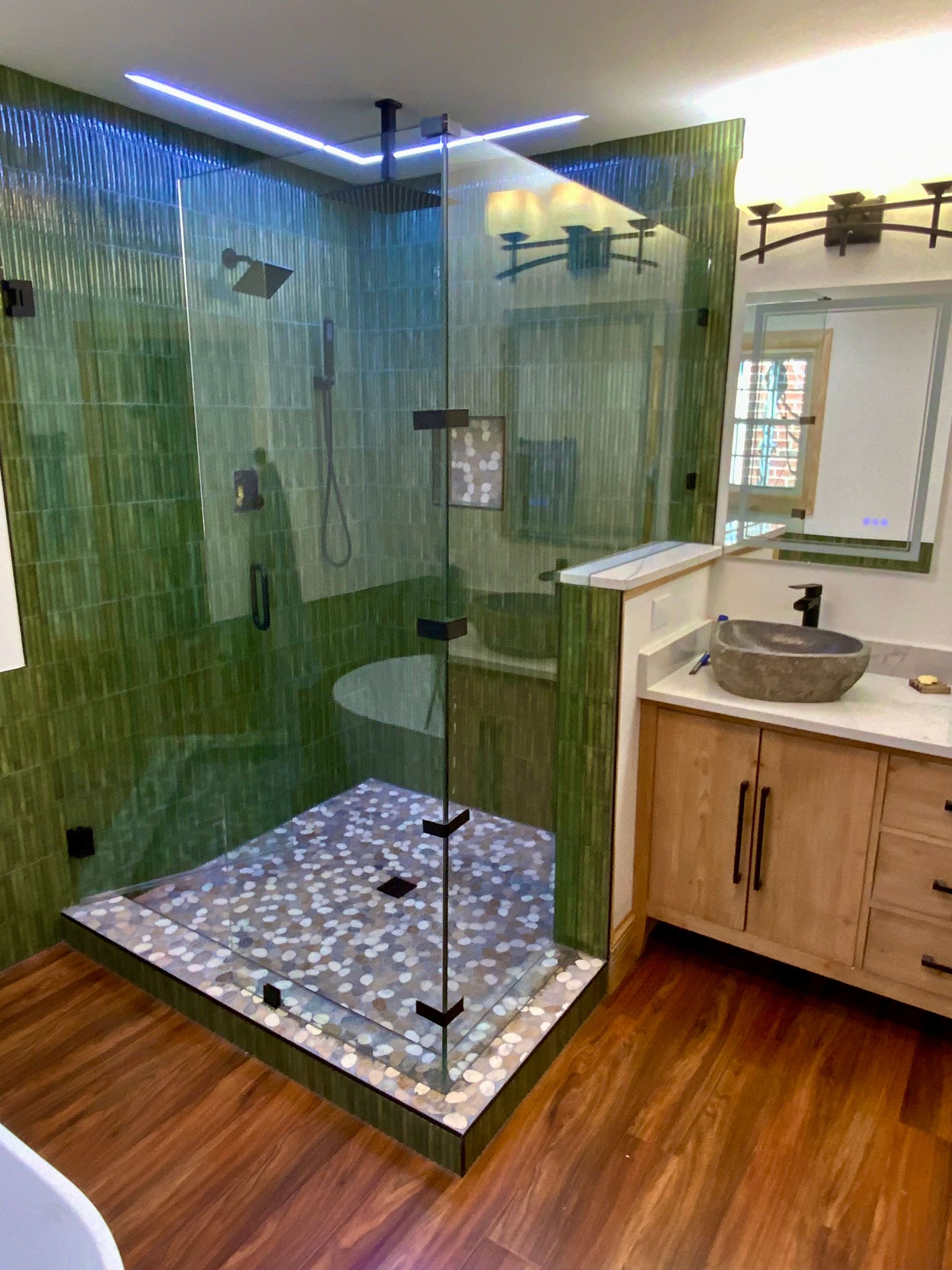 A bathroom with a walk in shower , sink , toilet and mirror.