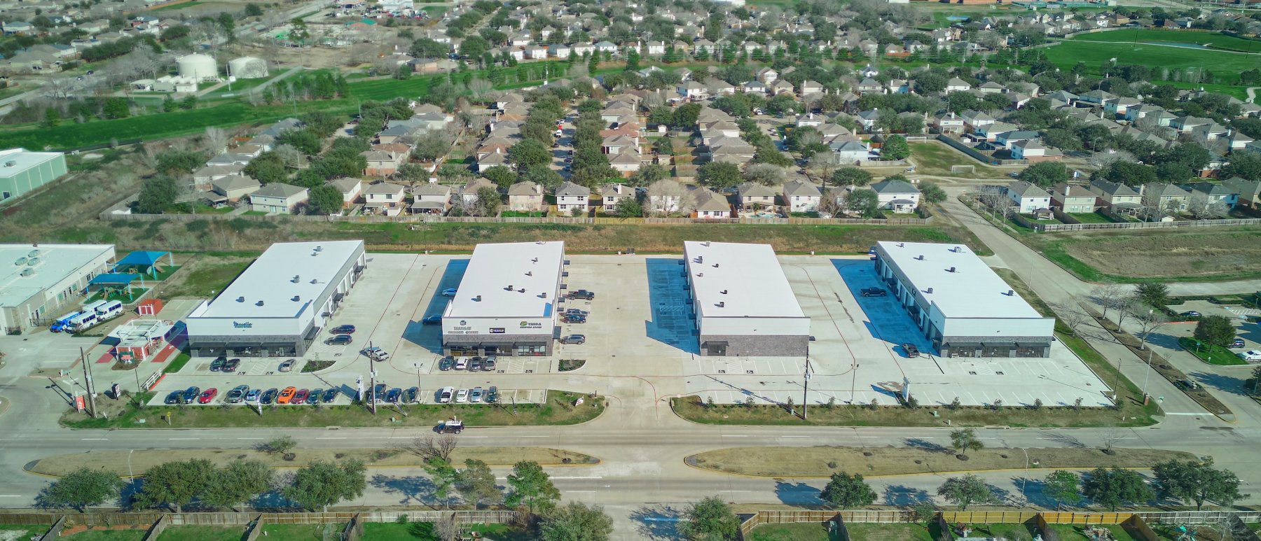 Aerial view of four industrial buildings surrounded by suburban homes and green spaces.