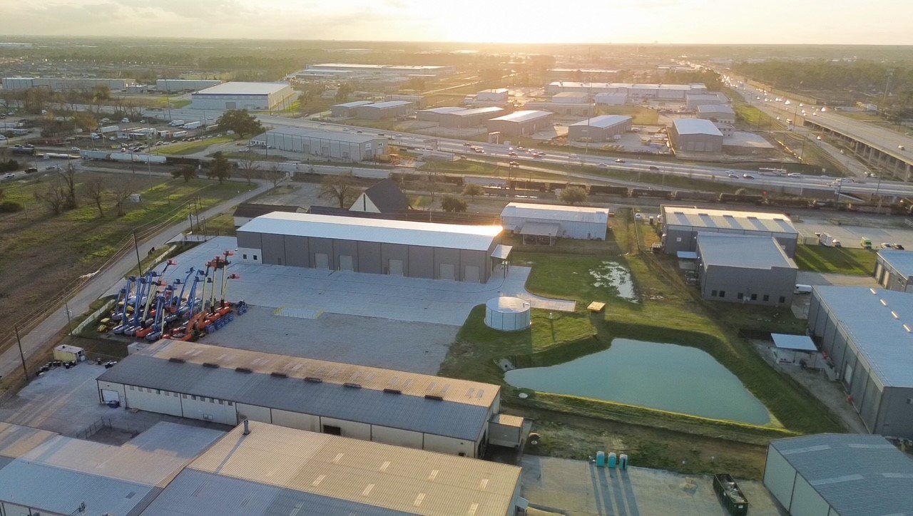 Aerial view of industrial buildings at sunset, with a pond and parked vehicles.