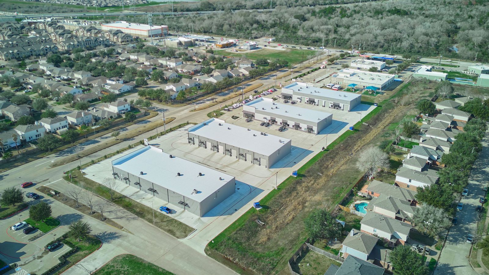 Aerial view of commercial buildings with parking, near residential housing and green space.