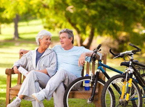 an elderly couple is sitting on a park bench next to bicycles .
