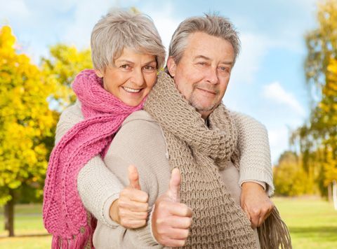 an elderly couple is giving a thumbs up in a park .