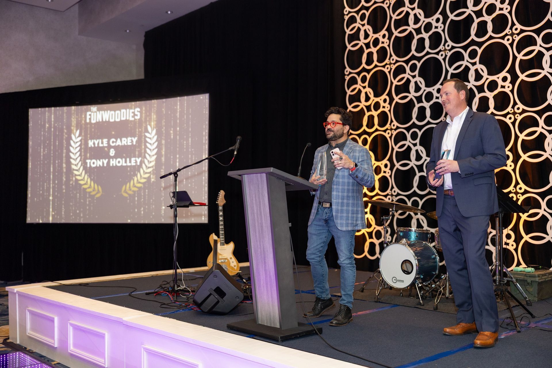Two men are standing on a stage in front of a podium.