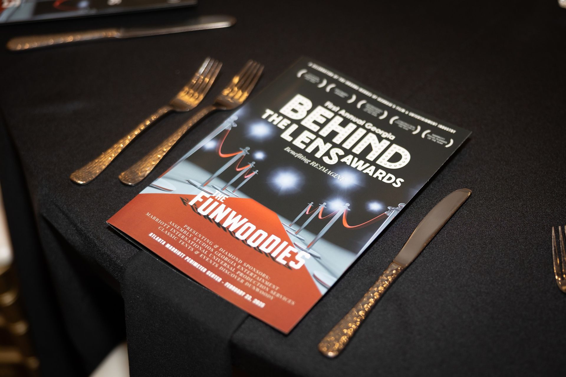 Behind the lens awards booklet on a table with silverware
