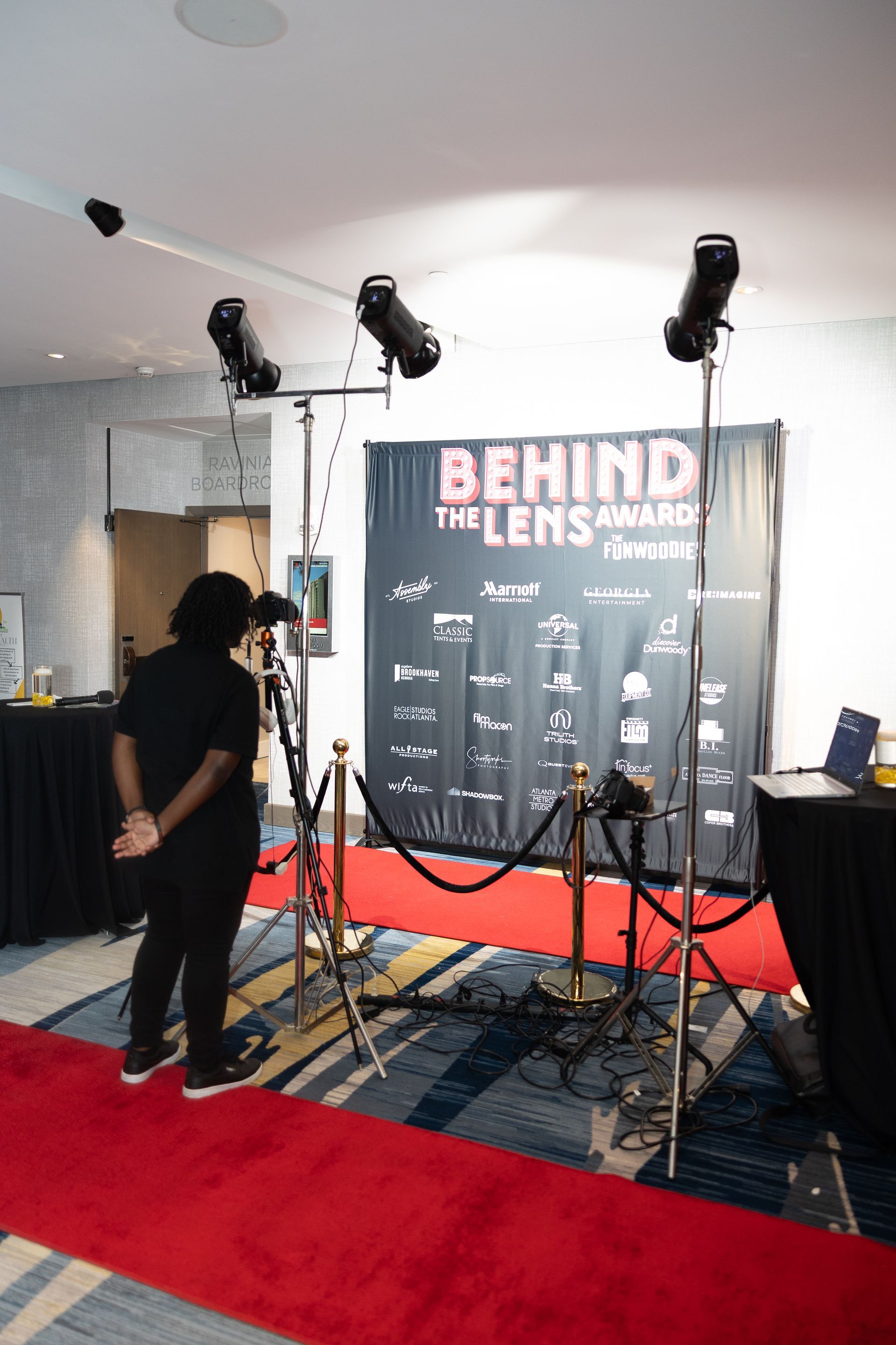 A man is standing on a red carpet in front of a sign that says behind the lens awards.