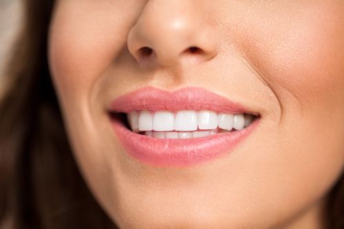 A close up of a woman's smile with white teeth and pink lips.