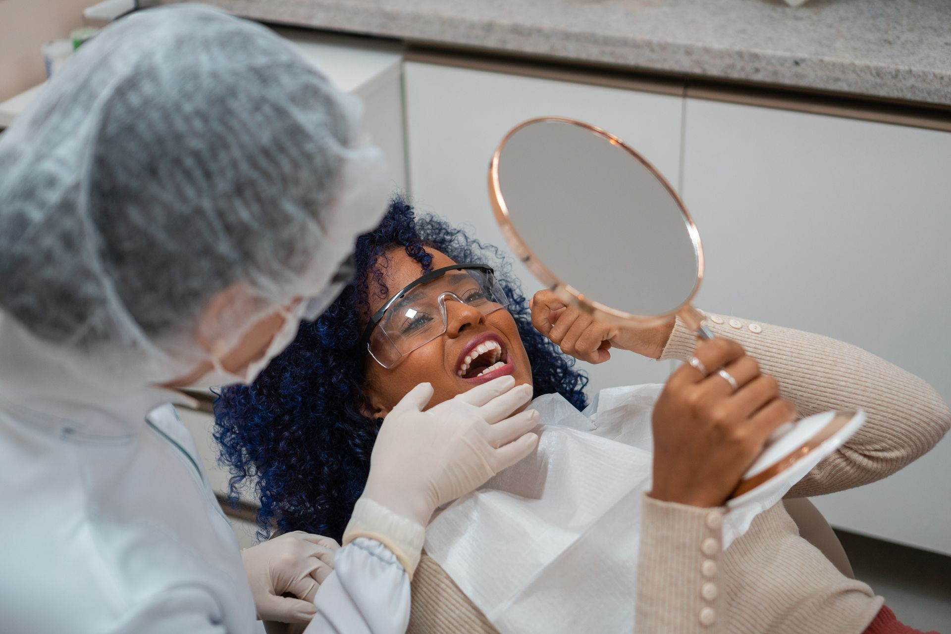 Smiling woman at dental office looking in mirror with dentist nearby Smiling woman at dental office looking in mirror with dentist nearby