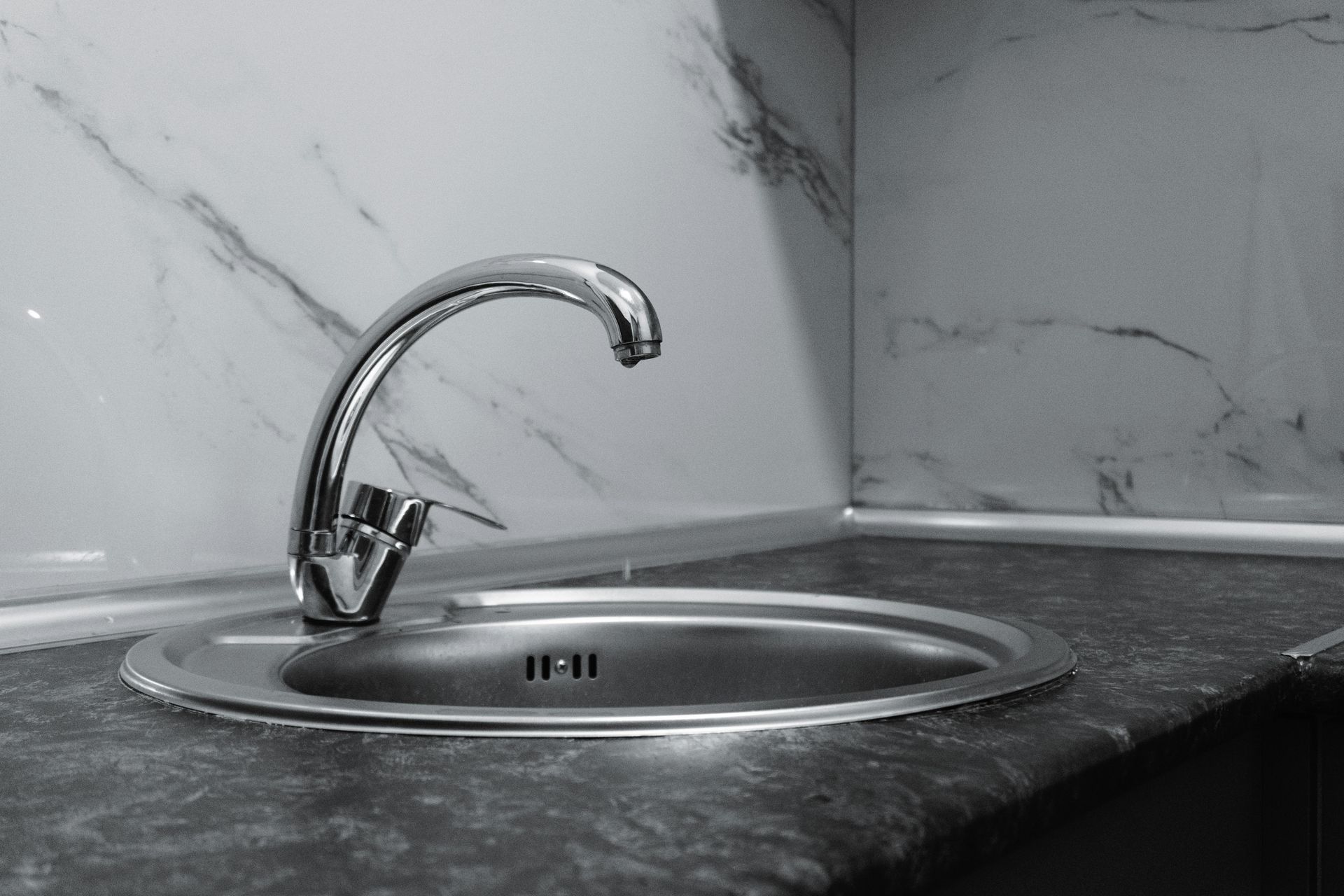 Silver faucet over a stainless steel sink in a kitchen with marble-patterned wall.