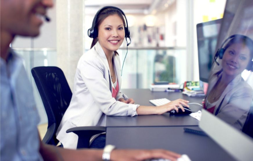 Una mujer con auriculares está sentada en un escritorio frente a una computadora.