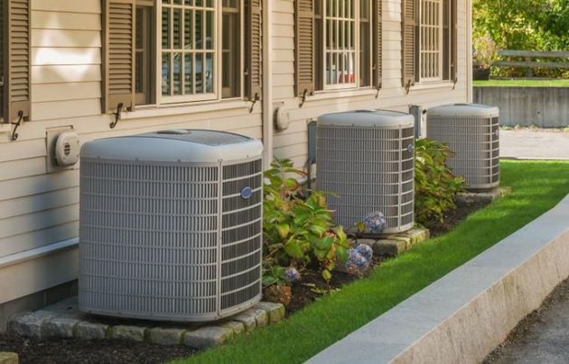 A row of air conditioners on the side of a house.