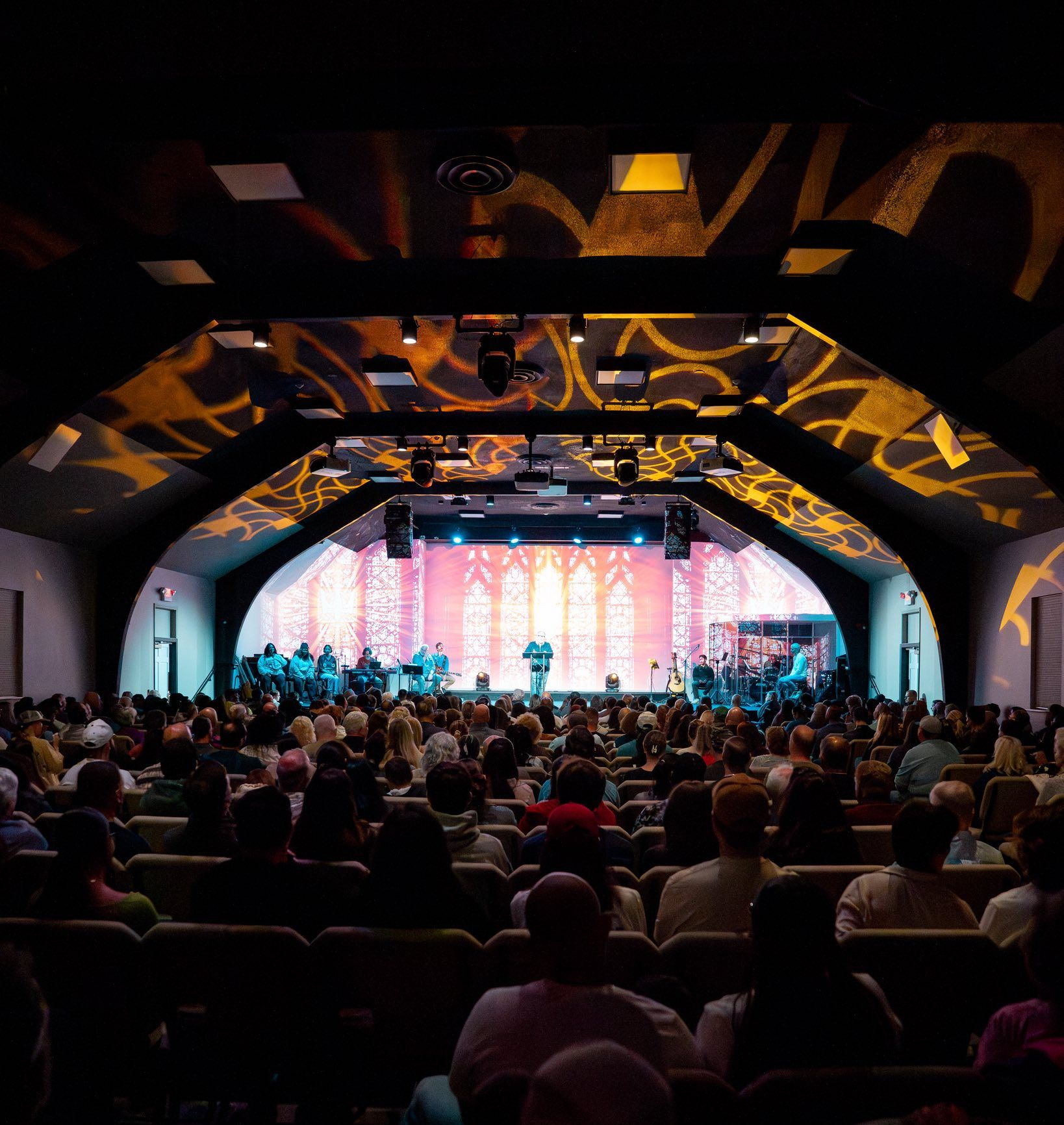 Worship service: People singing with raised hands, stage lit with blue and pink hues.
