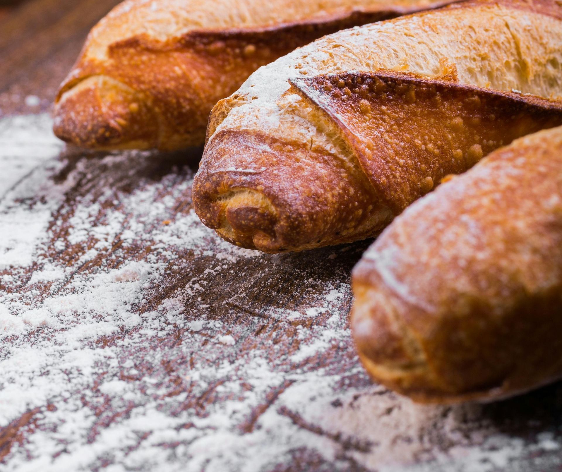 Three loaves of bread are sitting on a wooden table covered in flour.