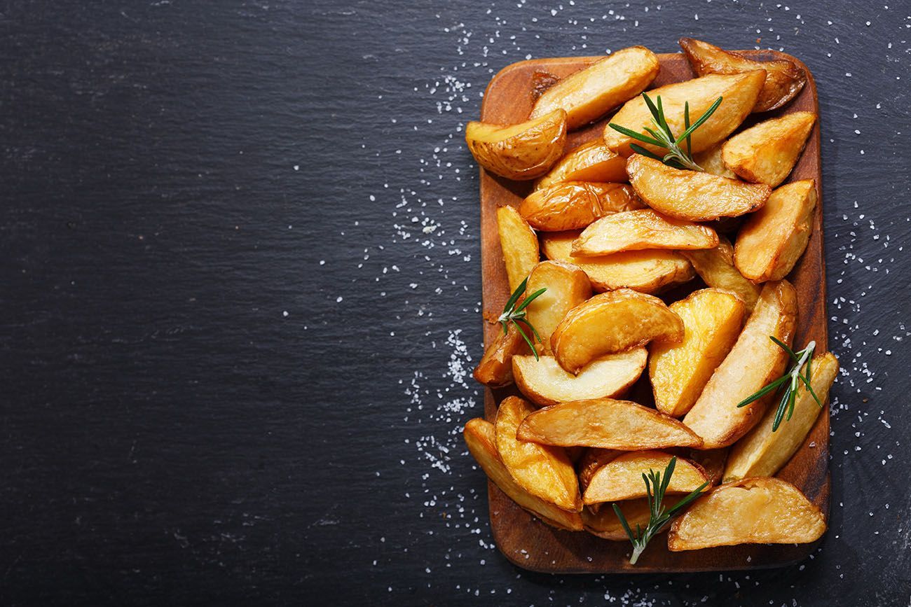 a wooden cutting board topped with potato wedges and rosemary