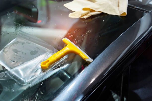 A yellow squeegee is sitting on top of a car window.