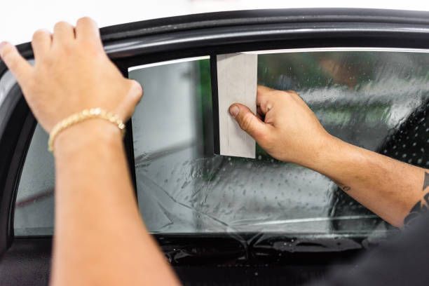 A person is applying tinted window film to a car window.