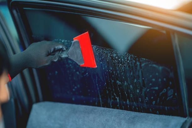 Guy applying window tint to a car with a red tool