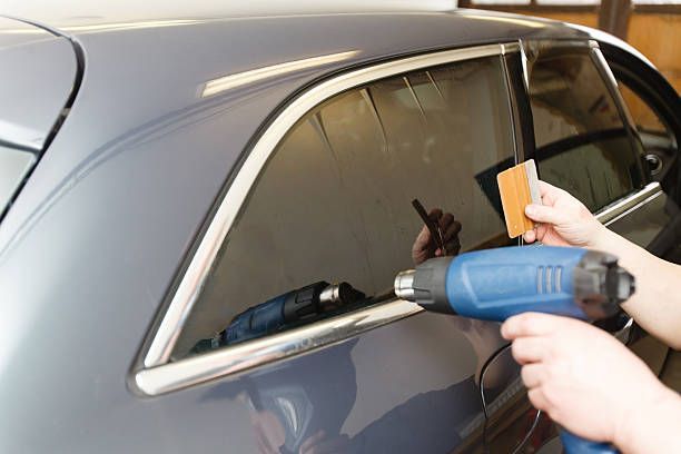 A person is applying tinted window film to a car window.