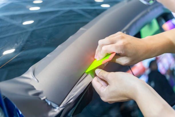 A person is wrapping a car with a yellow tool.