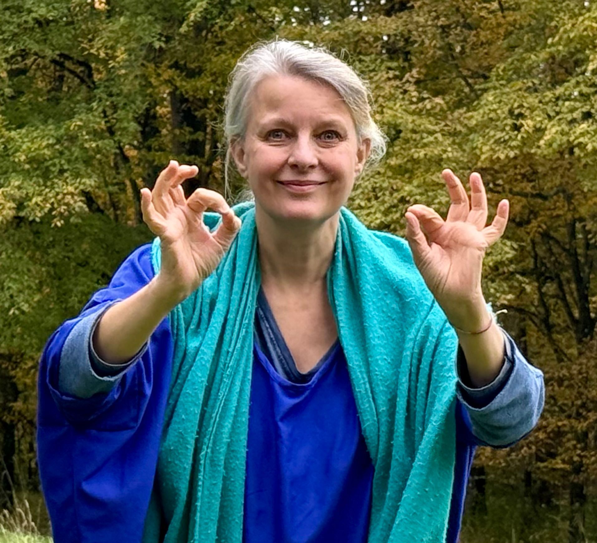 Femme souriante, regardant ailleurs, portant des vêtements bleus, debout près d'une fenêtre.