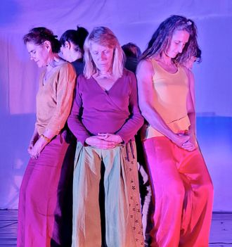 Une femme danse sur scène vêtue d'une robe bleue. Éclairage rose et violet.