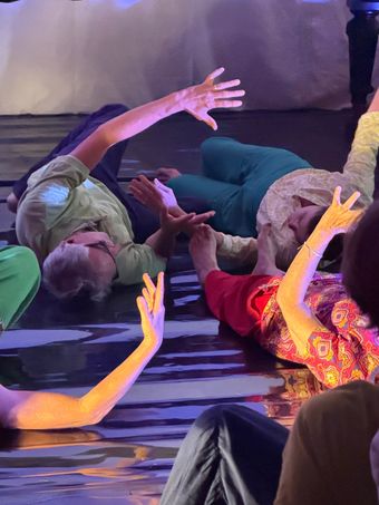 Femme en robe blanche, dansant sur scène avec un éclairage violet, ombre sur le mur.