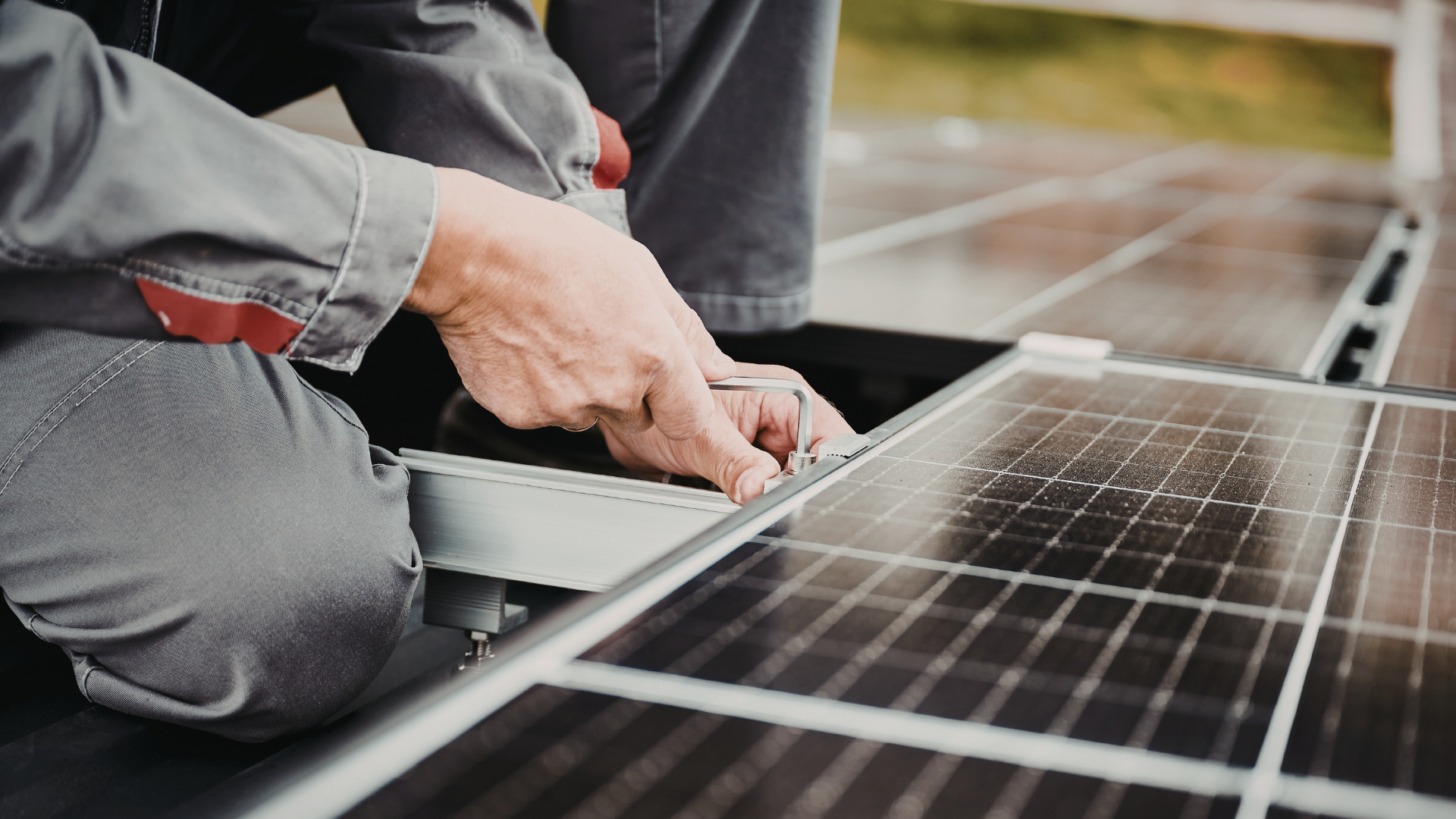 A technician in work clothes kneeling to install or maintain solar panels on a rooftop.
