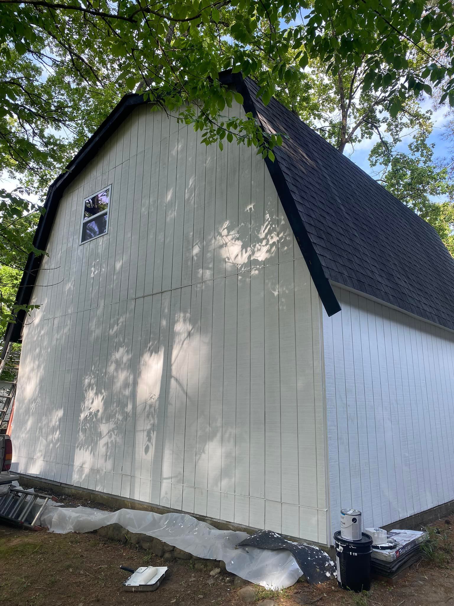 a white barn with a black roof is being painted .