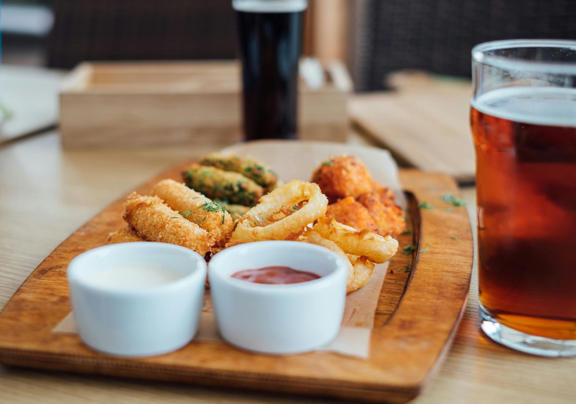 A wooden tray with fried food and a glass of beer on a table.