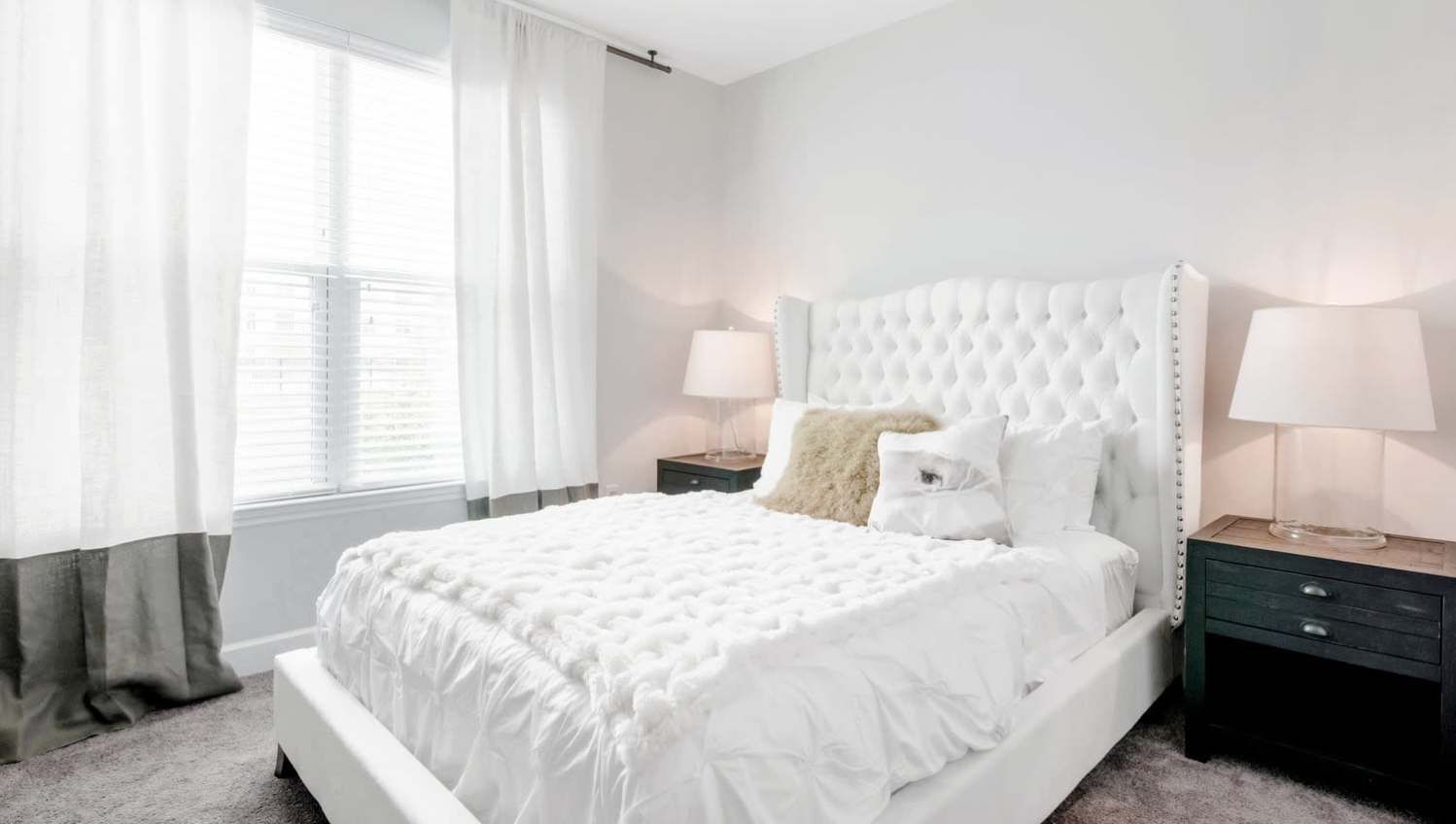 White bedroom with tufted headboard, white bedding, and two dark nightstands with lamps.
