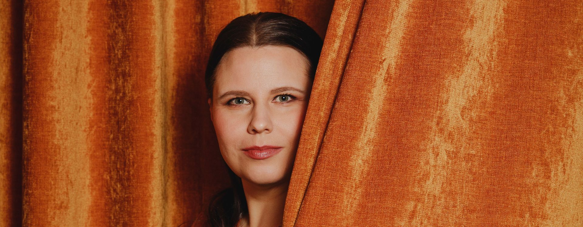 Kirjailija Helena Immonen kurkistaa verhon takaa.