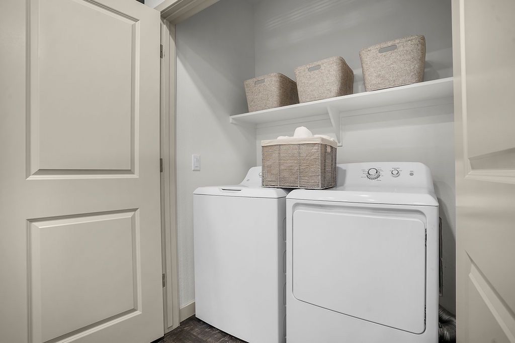 White washer and dryer side by side in a laundry closet with baskets on a shelf.