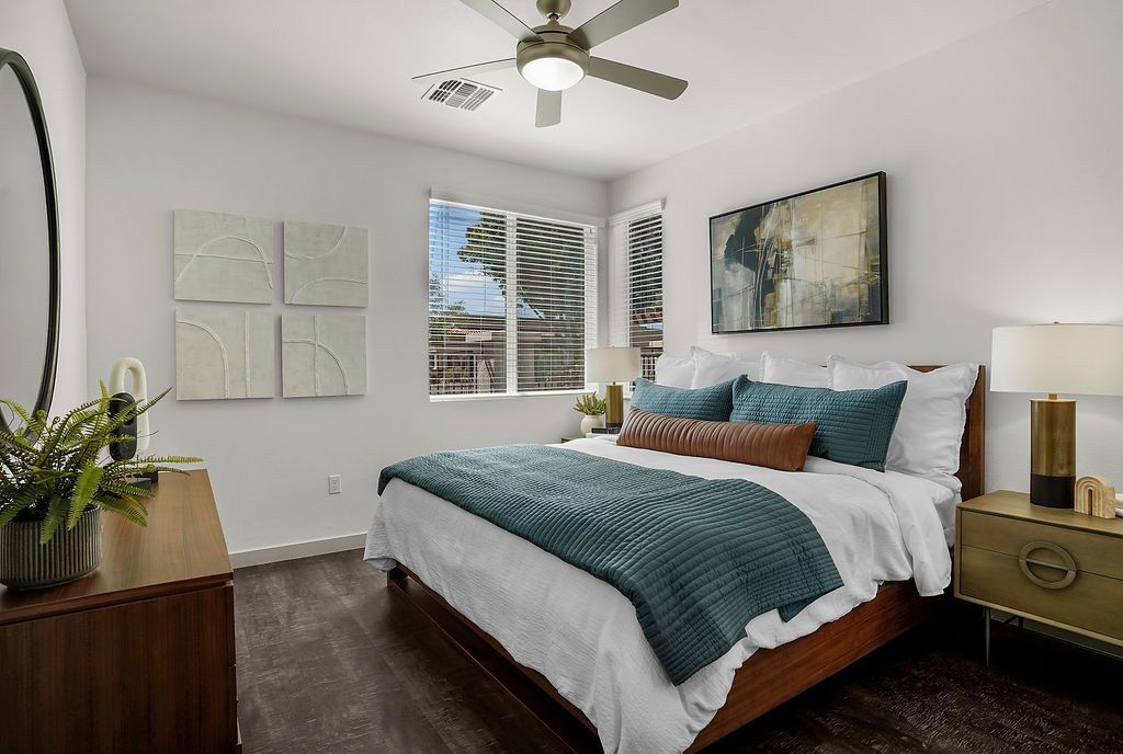 Bedroom in a modern apartment with a wooden bed, teal quilt, white linens, and window blinds.