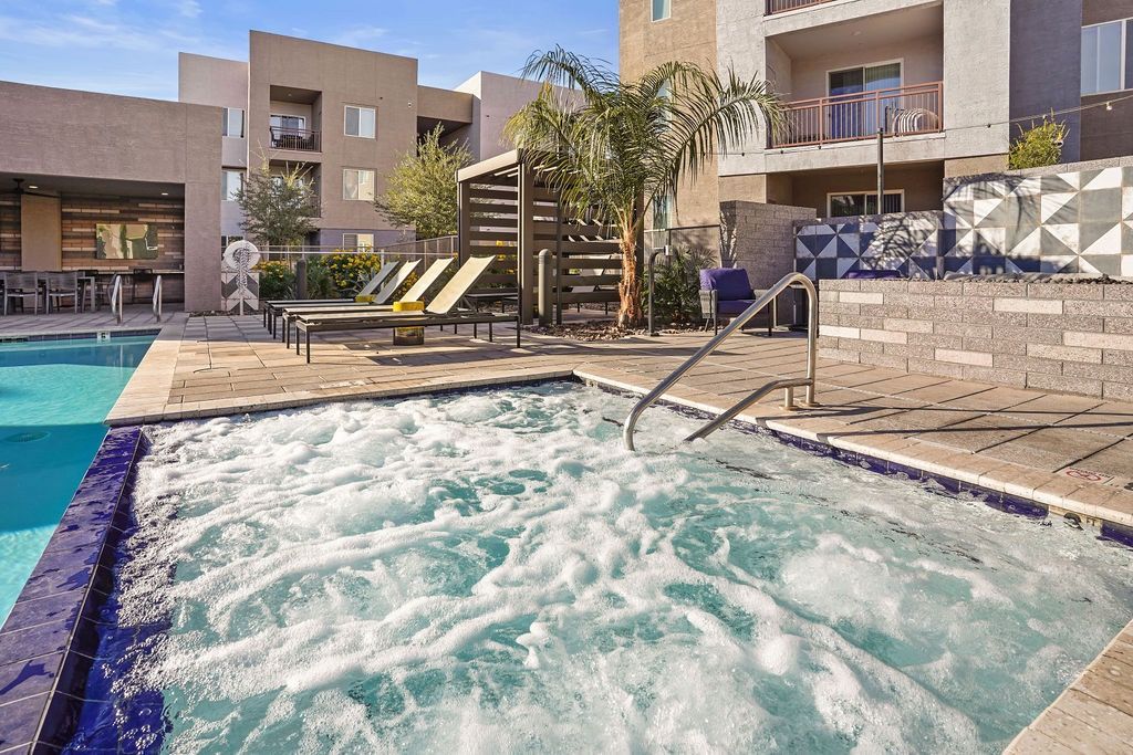 Outdoor community pool with steps, a metal handrail, and lounge chairs on a stone deck.