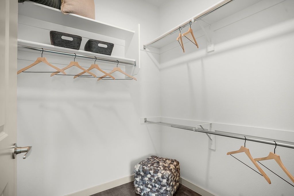 Walk-in closet with hanging rods, shelves, baskets, and a cushioned pouf.