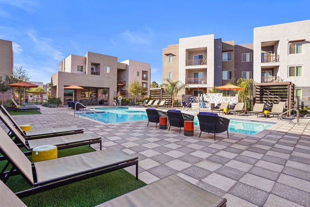 Outdoor pool area with lounge chairs, umbrellas, and surrounding apartment buildings.