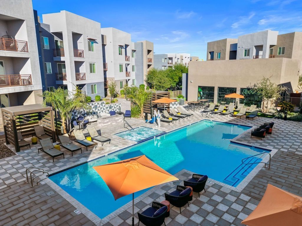 Outdoor pool at a multi-family complex with lounge chairs and orange umbrellas.