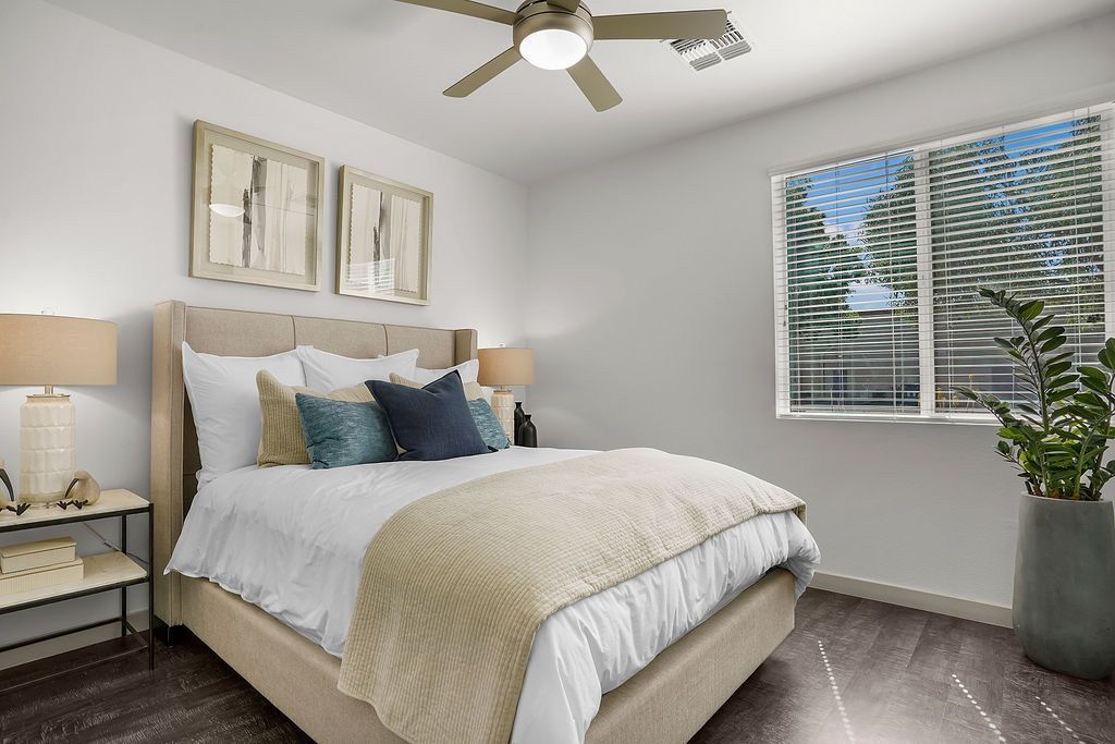 Bedroom in a modern apartment with a beige upholstered bed, two nightstands, lamps, and a large window.