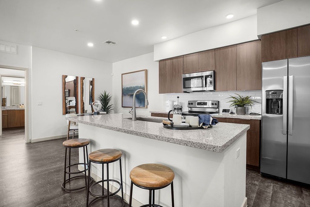 Open-concept kitchen with granite island, stainless-steel appliances, and three bar stools.