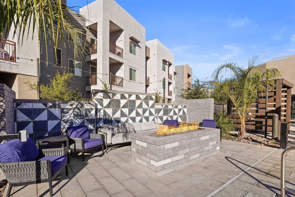 Outdoor lounge with a rectangular gas fire pit, cushioned seating, and a geometric tiled wall.