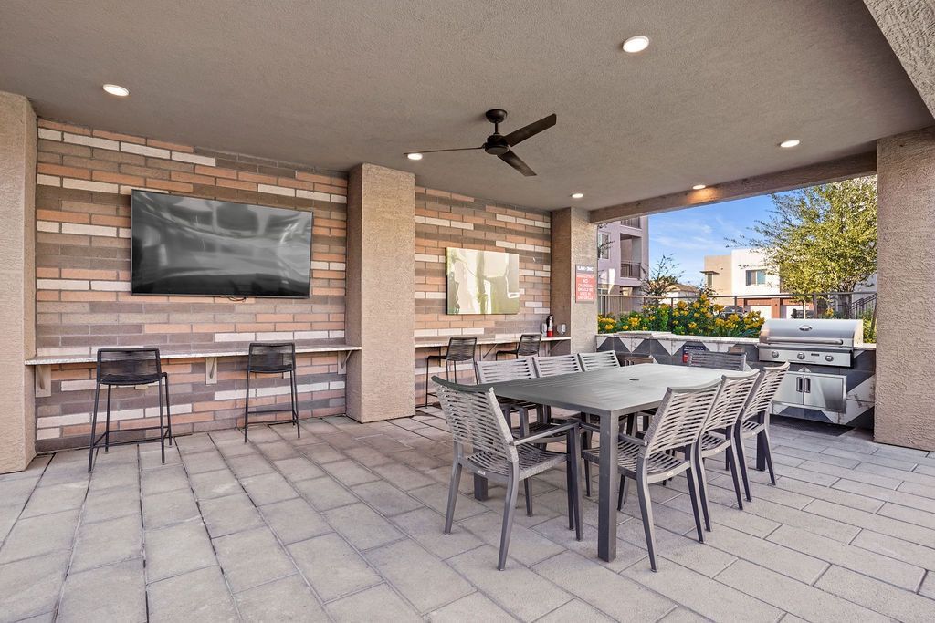 Covered outdoor resident amenity area with TV, grill, and communal dining table