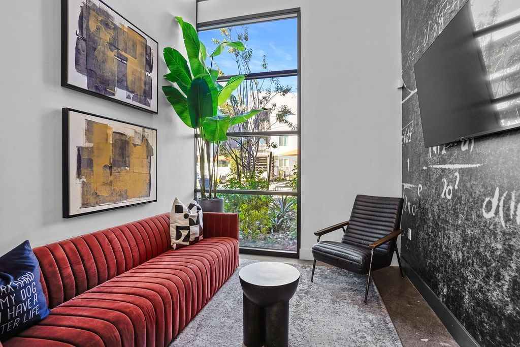 Interior community lounge with a red sofa, black chair, artwork, plants, and a large window.