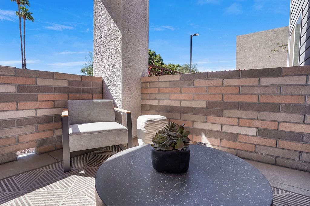 Outdoor balcony with a gray chair, round speckled table, and a succulent plant against brick walls.