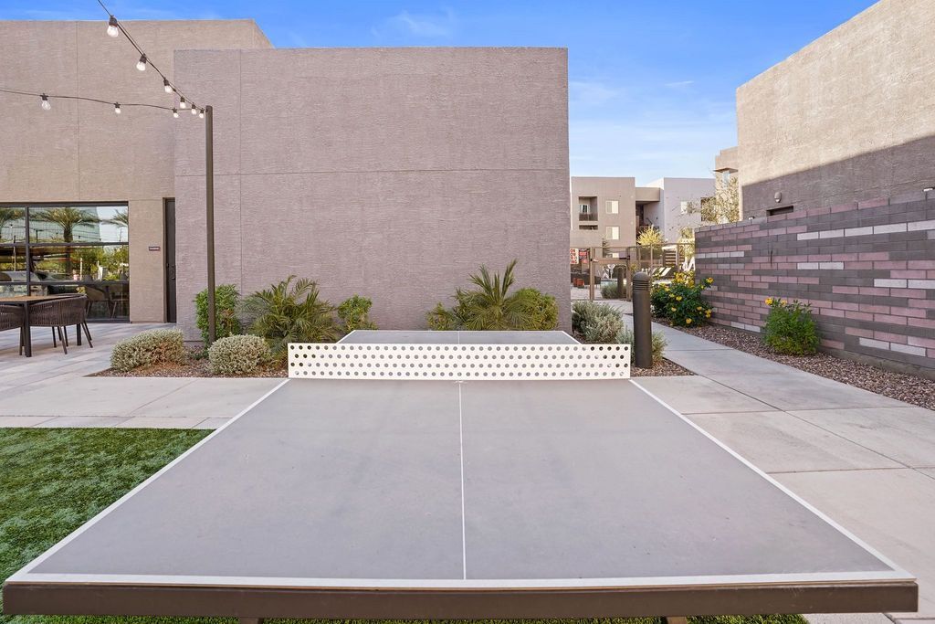 Outdoor communal area with a ping-pong table, string lights, and modern beige buildings.