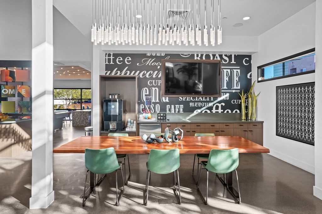 Bright community lounge with a long wooden table, green chairs, wall art, and a mounted TV.