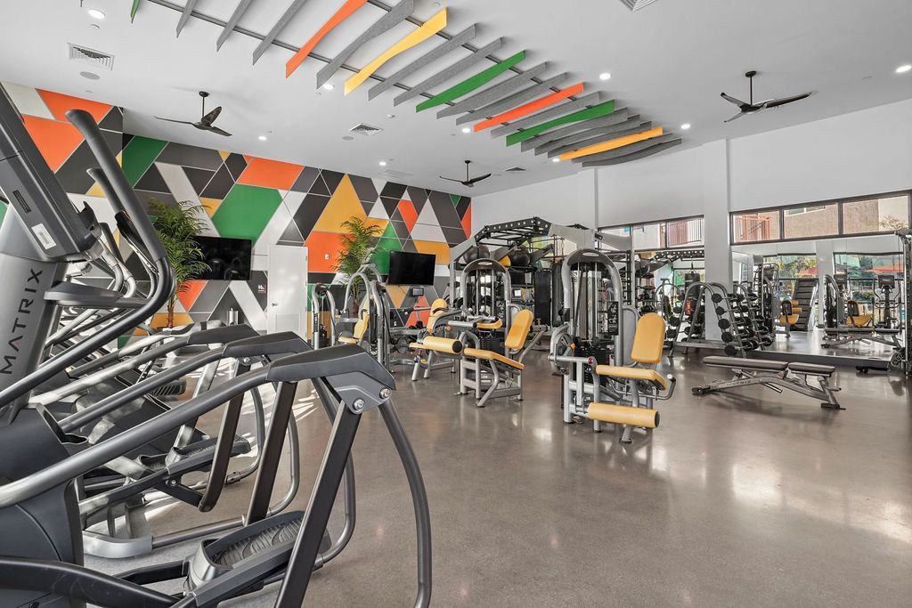 Spacious community gym with cardio and strength machines, colorful geometric wall art, and large mirrors.