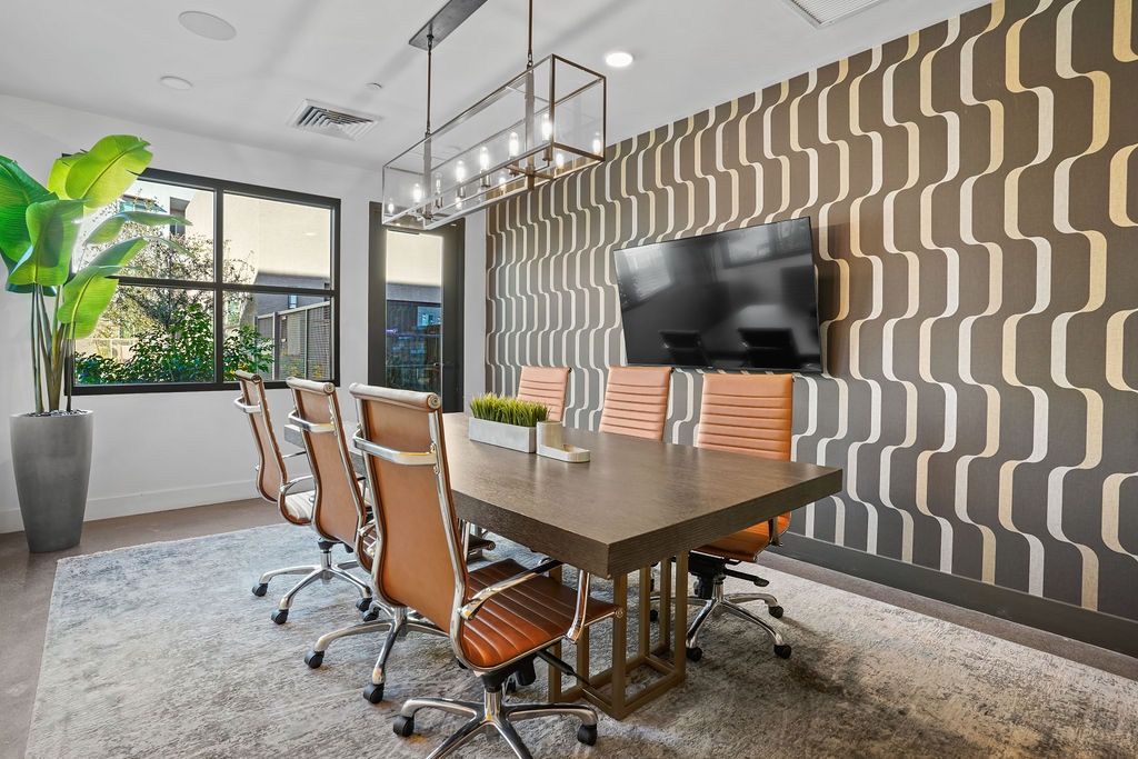 Modern conference room with a large table, orange swivel chairs, a wall-mounted TV, and patterned wallpaper.