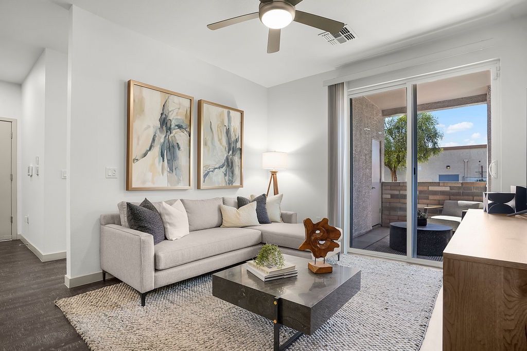 Bright apartment living room with a gray sofa, coffee table, abstract art, and sliding door to a balcony.