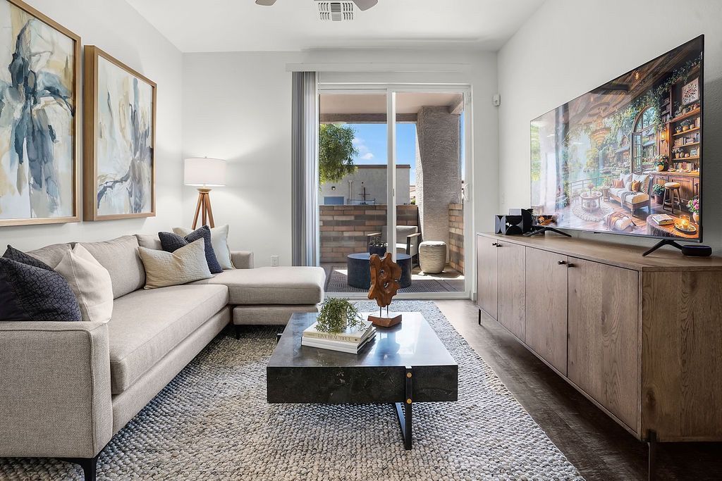 Living room in an apartment with a beige sectional, coffee table, wall art, and a wooden TV console.